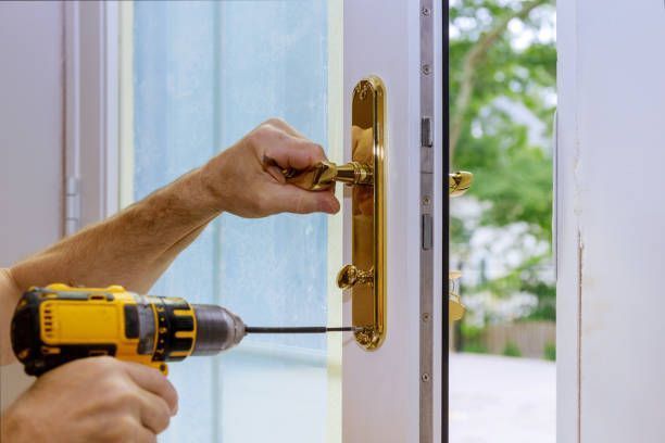 A person uses a yellow electric drill to install a brass door handle on a white door frame.