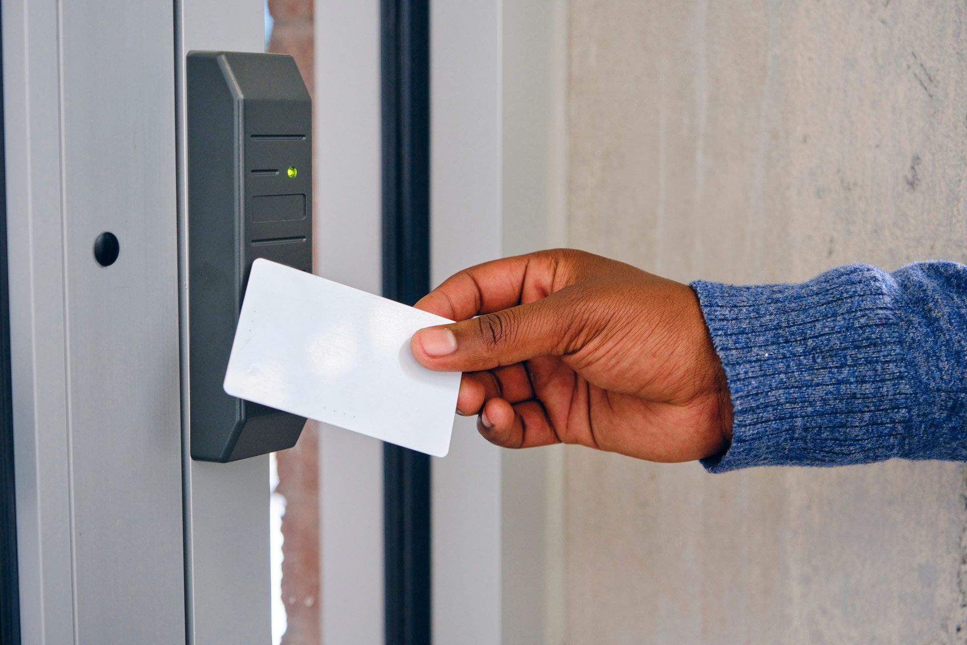 A hand holds a blank white key card near an electronic security scanner mounted on a door frame.