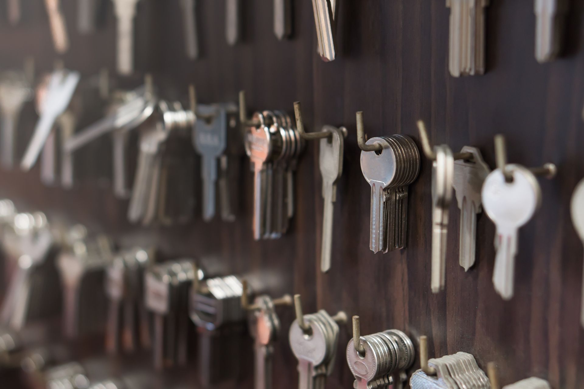 Rows of metal keys organized and hanging on hooks against a dark wooden display board.