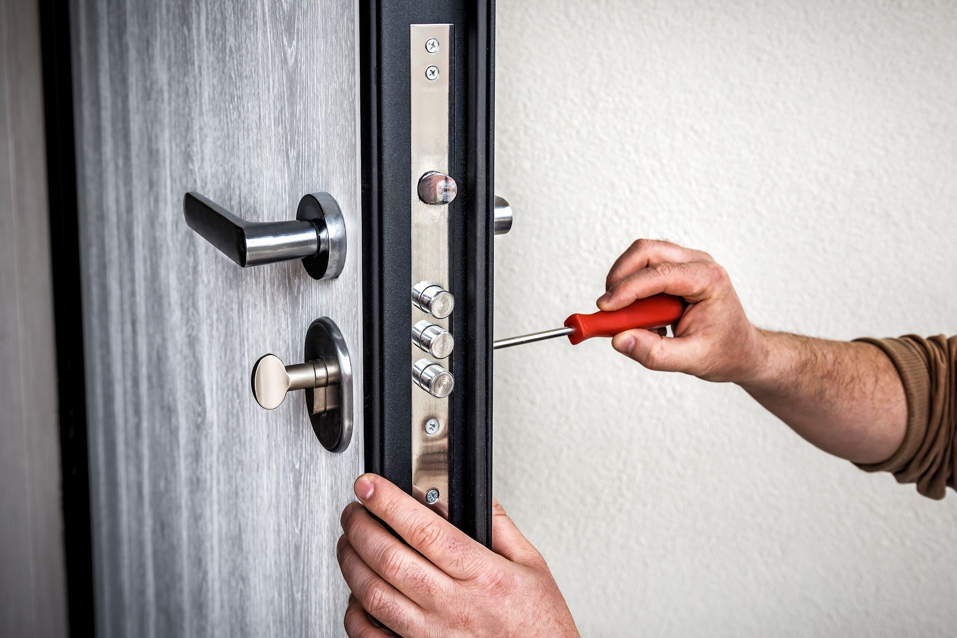A person using a screwdriver to adjust a door's lock mechanism.