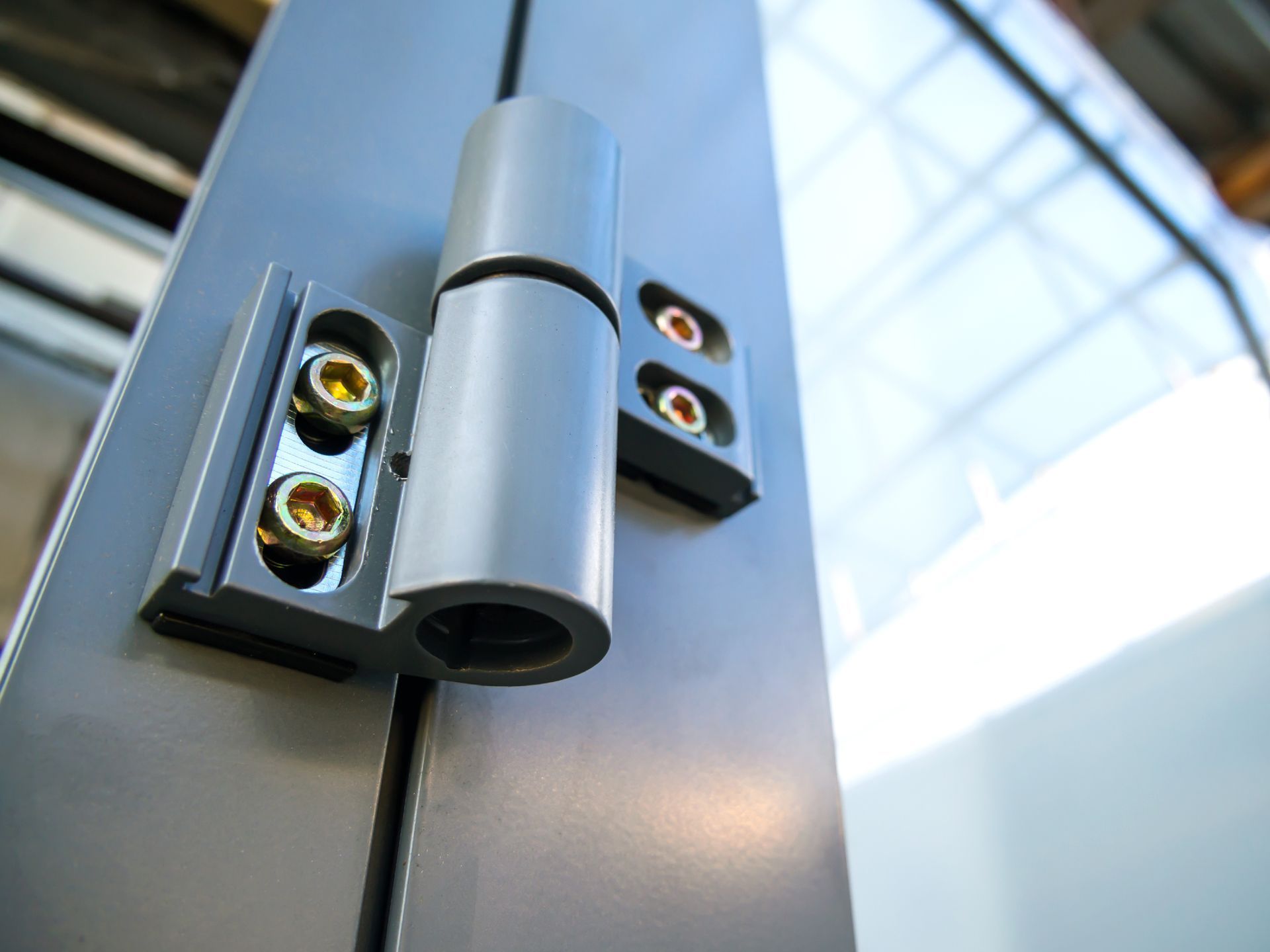 A white door with a silver multi-bolt locking mechanism and a key inserted in the lock, with a blurry outdoor background.