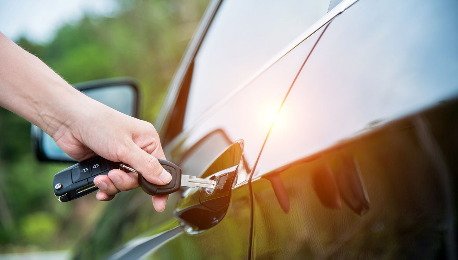 A hand holding a car key fob near the door handle of a black vehicle.