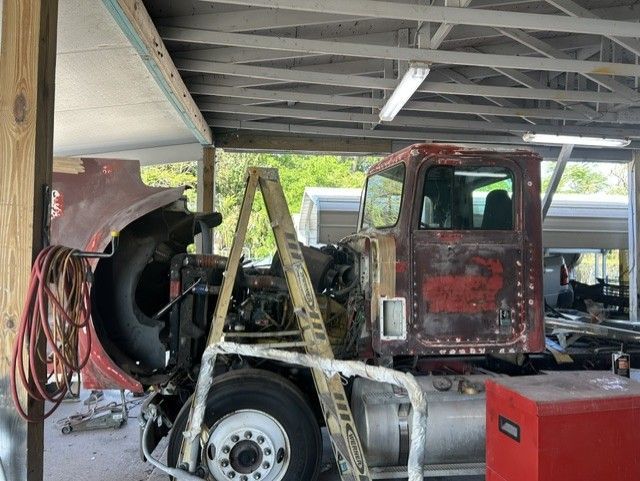 Red truck cab under repair in a garage, with a ladder, tools, and a large fan nearby