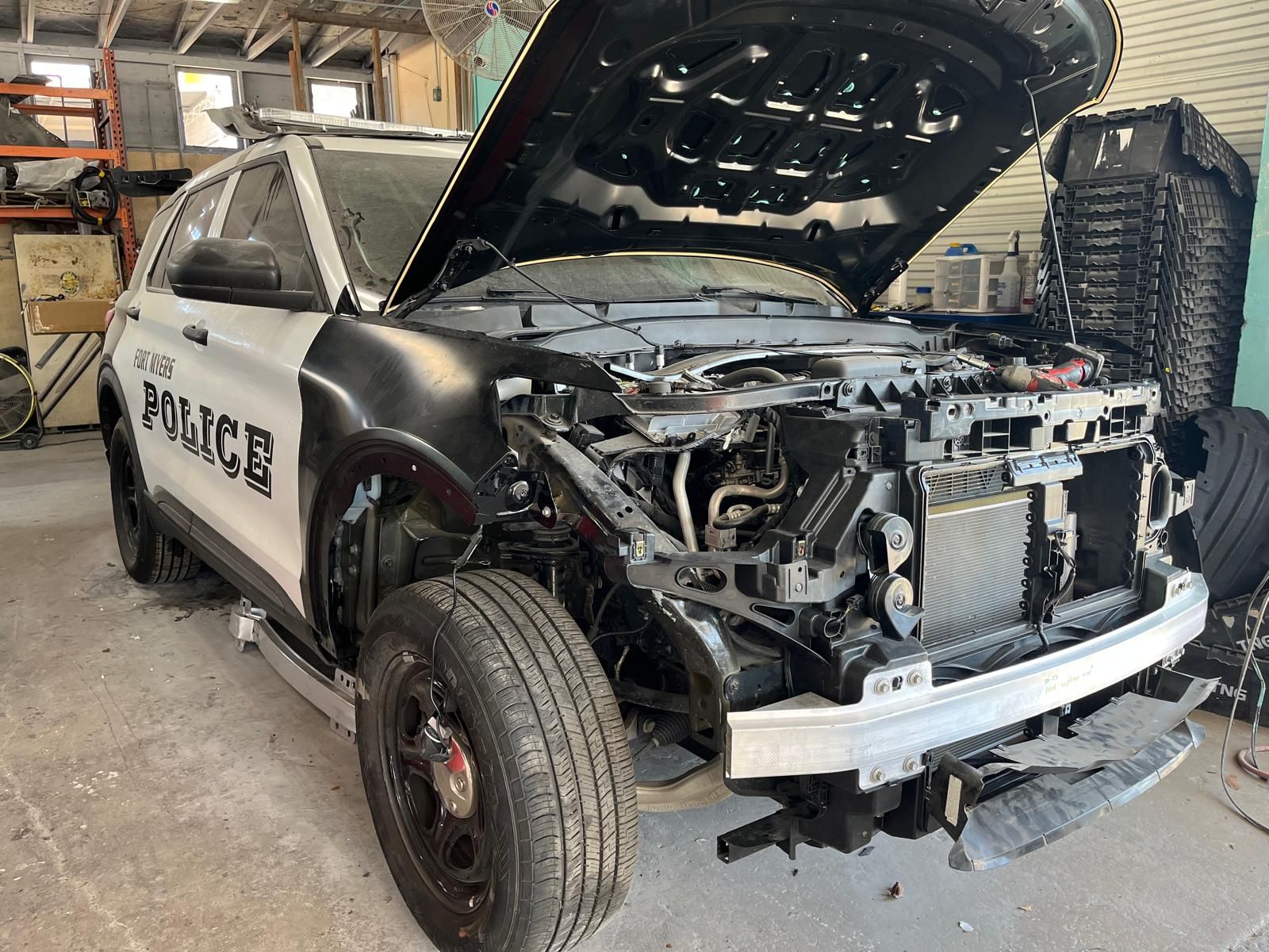 A police car with the hood open is sitting in a garage.