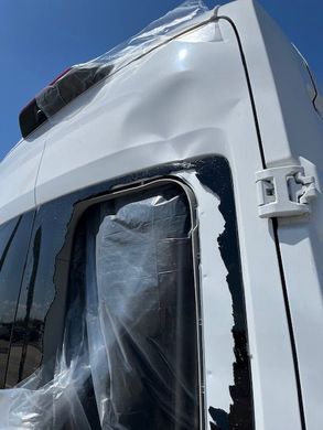 A white van with a broken window and a plastic cover on it