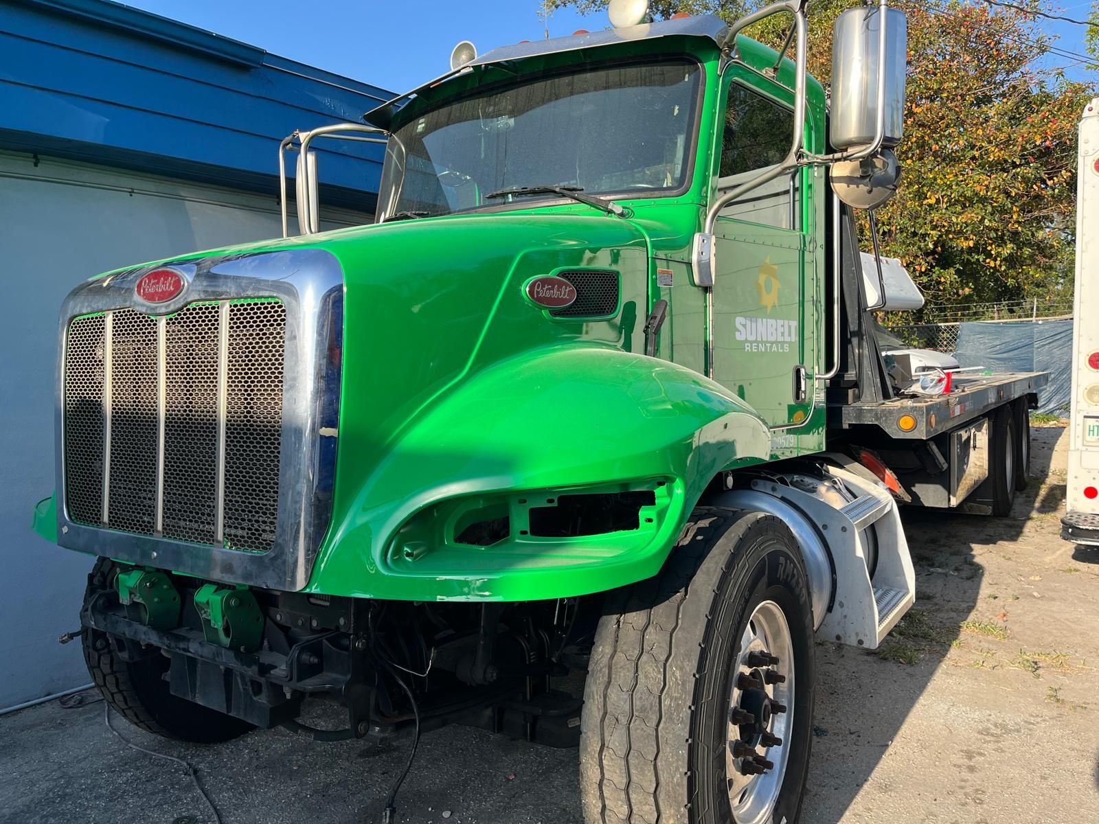 A green semi truck with a flatbed trailer is parked in front of a building.