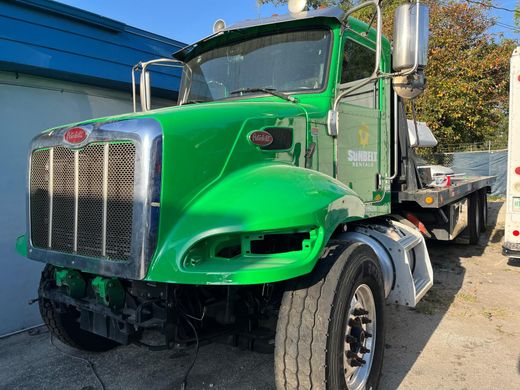 A green semi truck with a flatbed trailer is parked in front of a building.