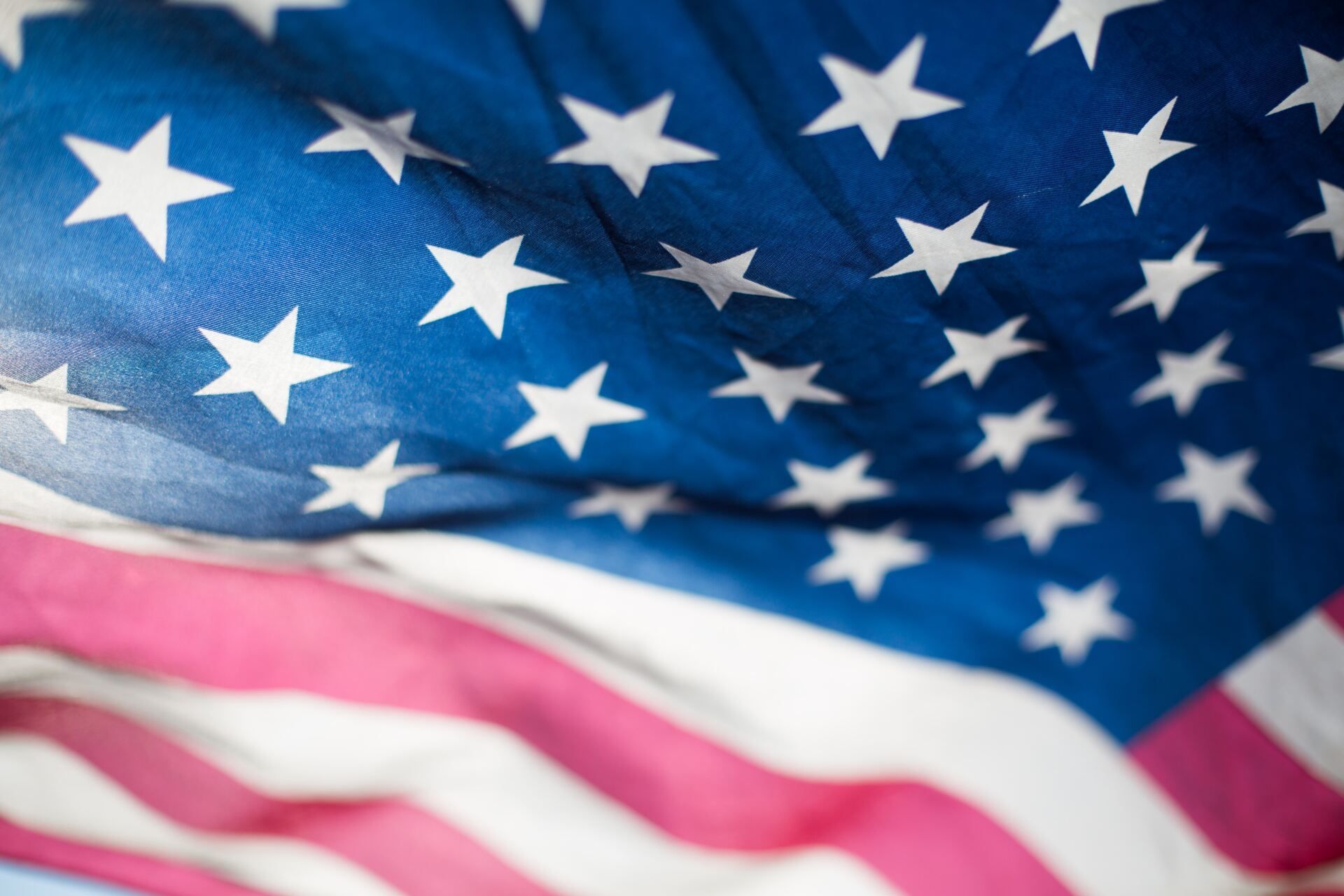 A close-up, angled view of a waving American flag, featuring bright white stars on a blue field and red and white stripes.
