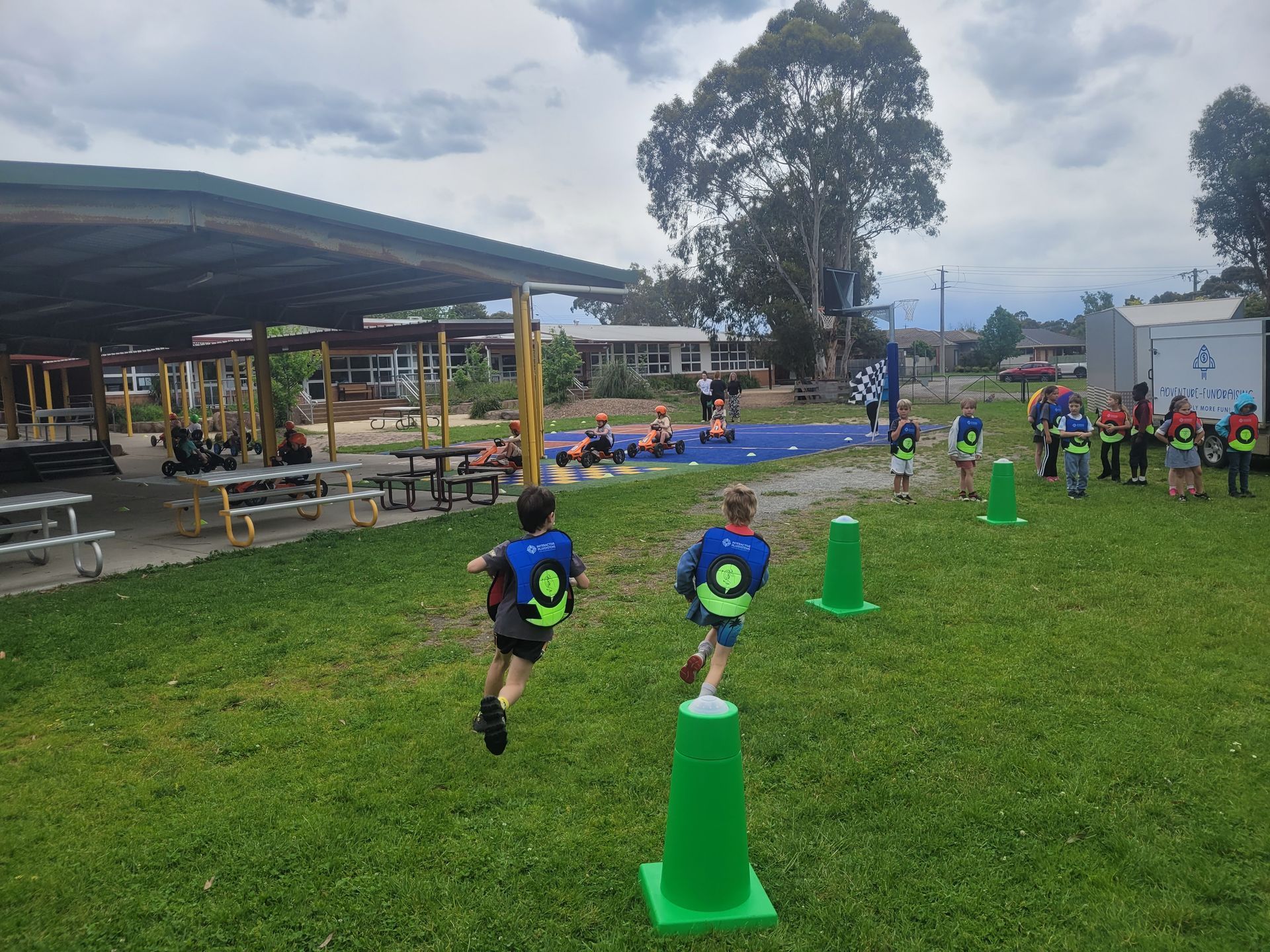 Two children running through green cones during an outdoor event at a school.