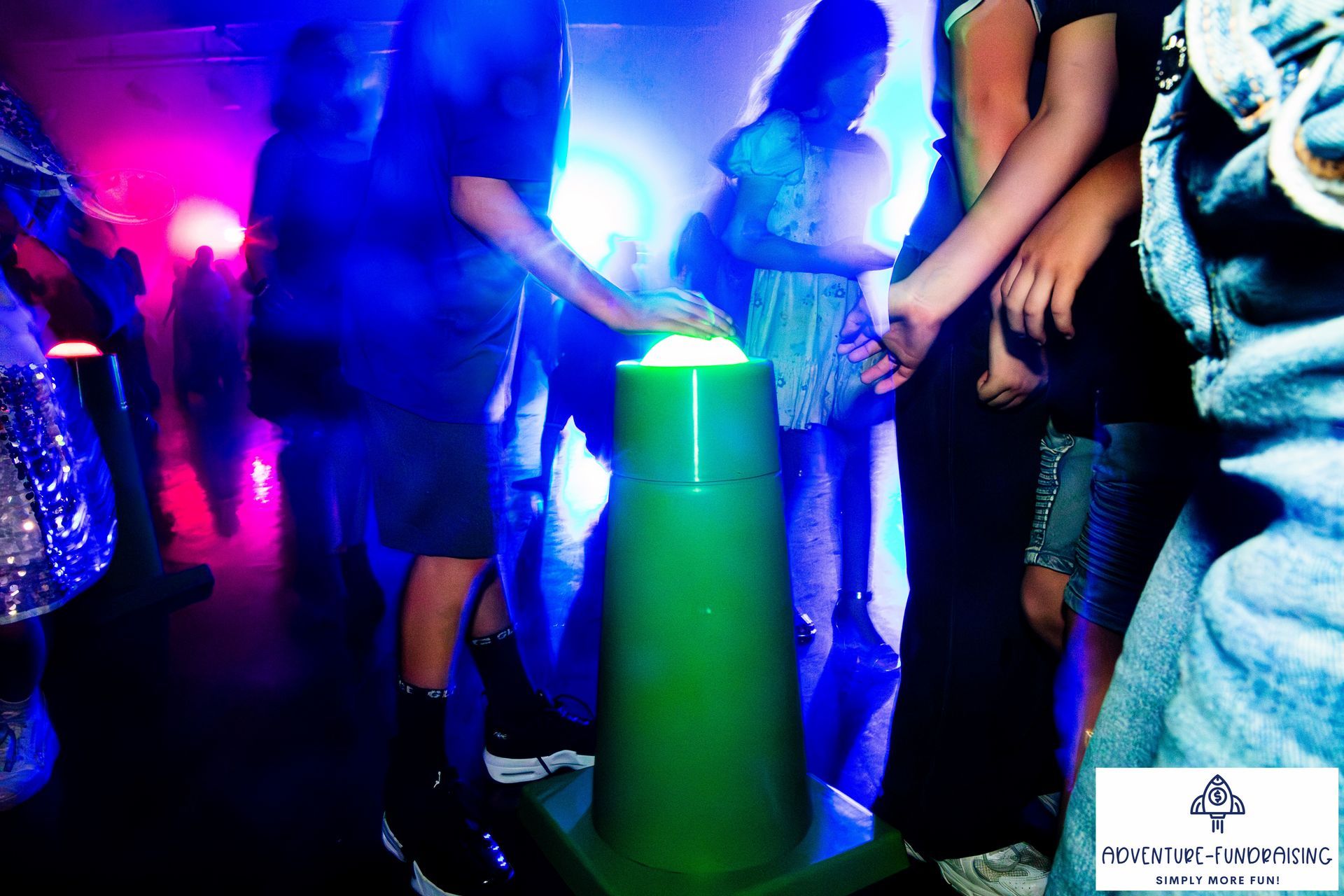 People gathered around a glowing green cone, illuminated by blue and pink lights.