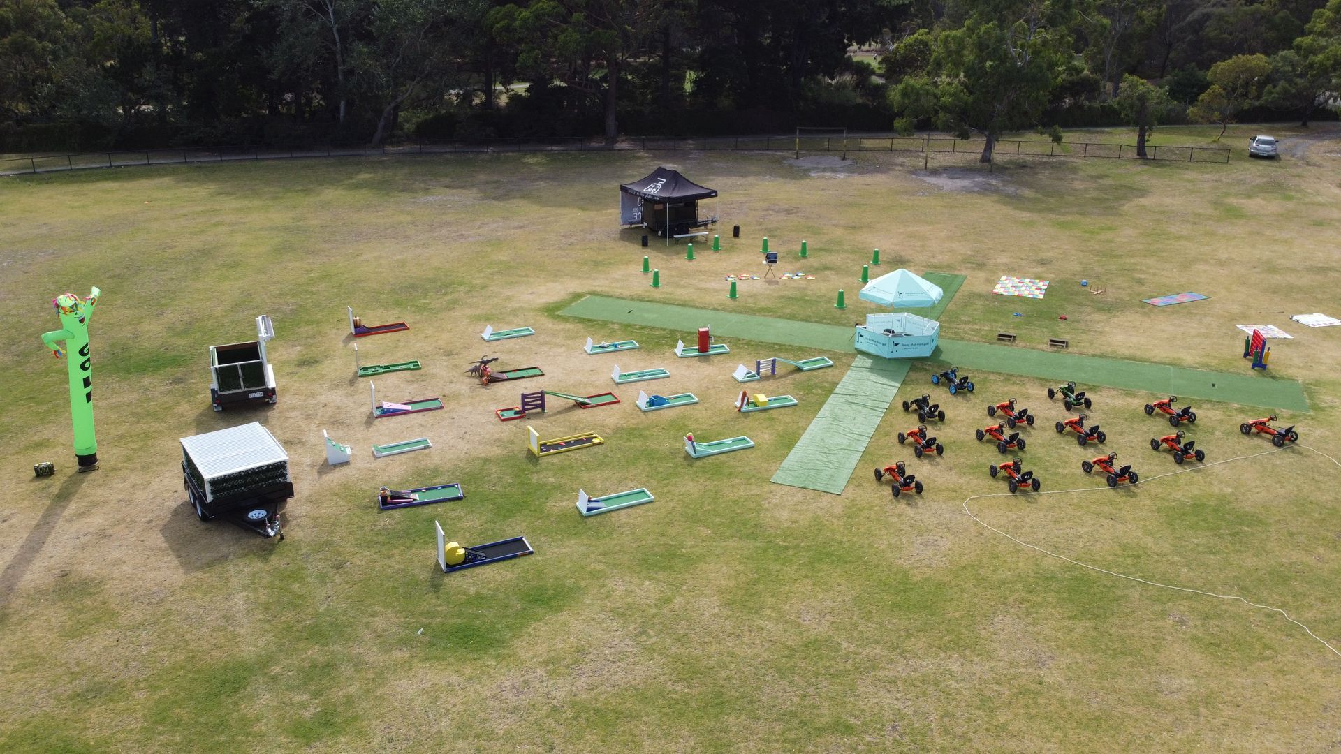 Overhead view of a grassy field with people doing yoga, plus tents, inflatable figures, and small vehicles.