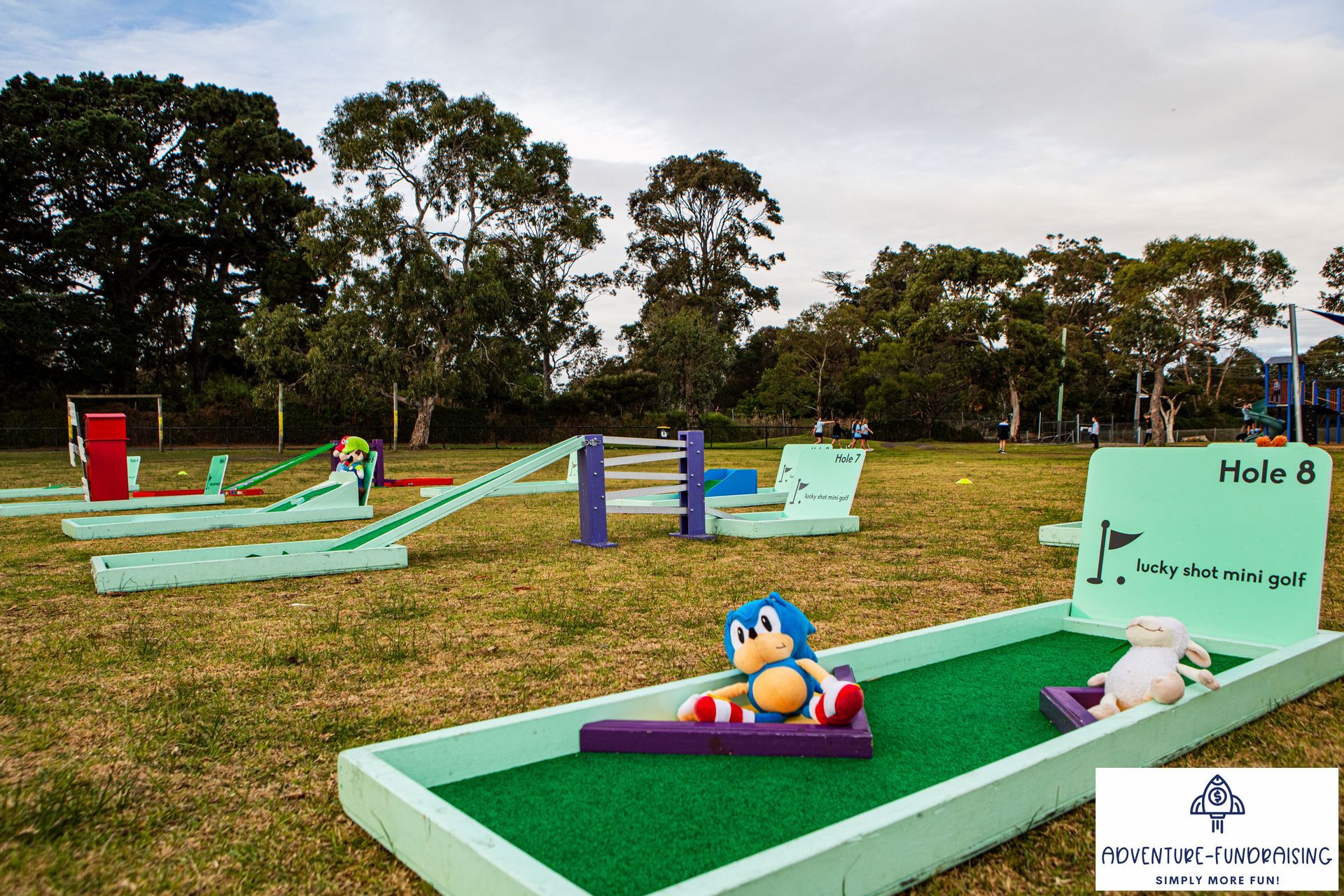 Mini golf course with green and purple obstacles, Sonic toy on a ramp, lamb toy near hole 8 sign.