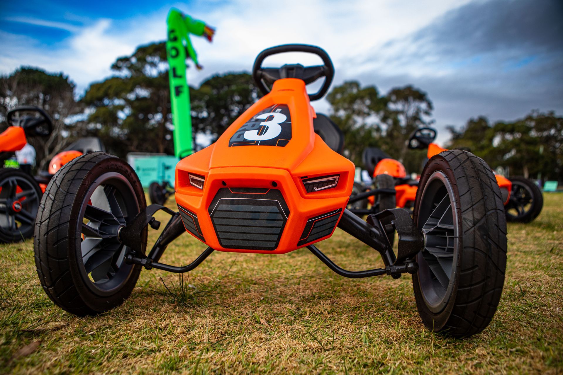 Orange pedal go-kart with the number 3, black tires, and steering wheel, on a grassy field.