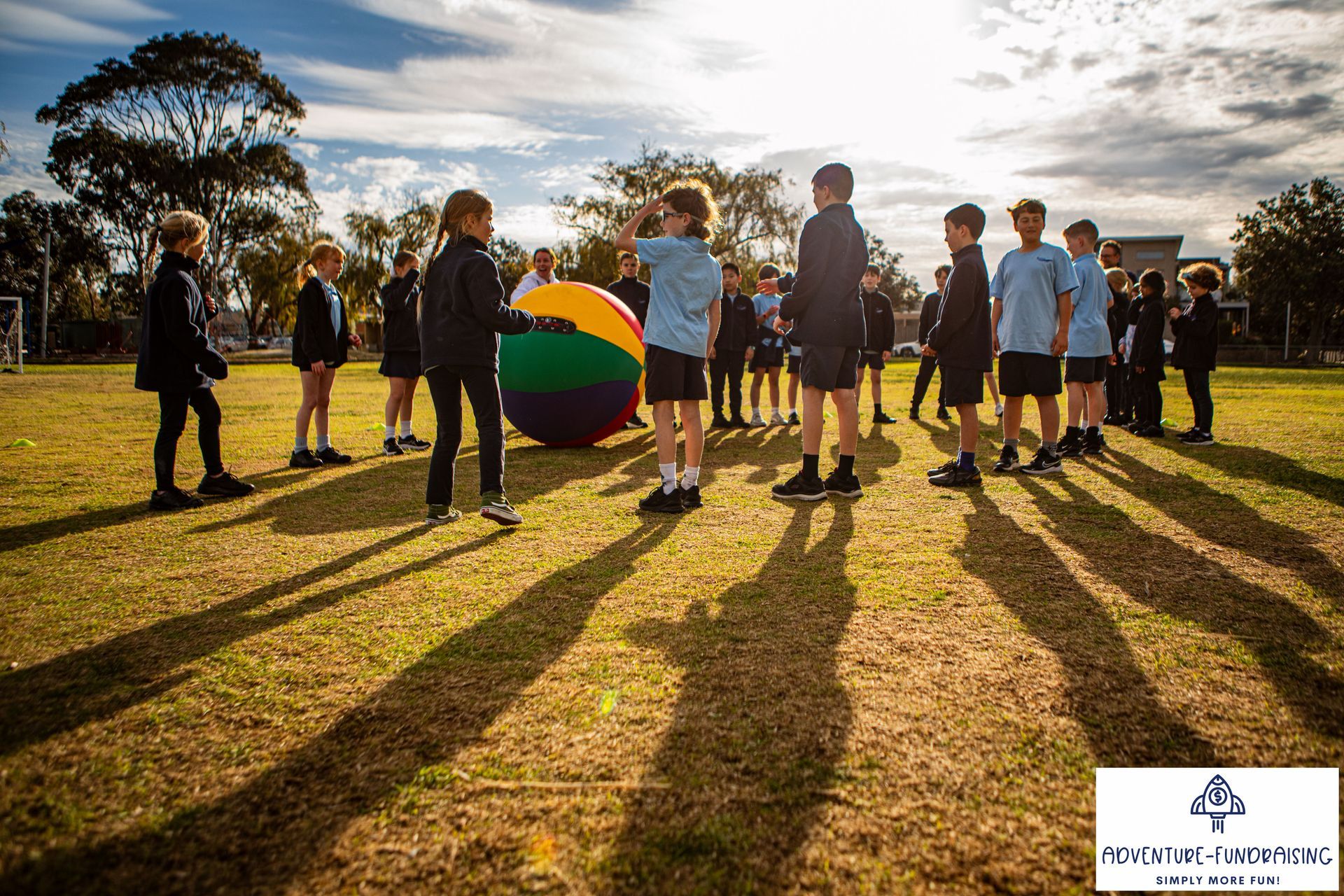 Students in school uniforms on a grassy field with a large ball, preparing to play a game.