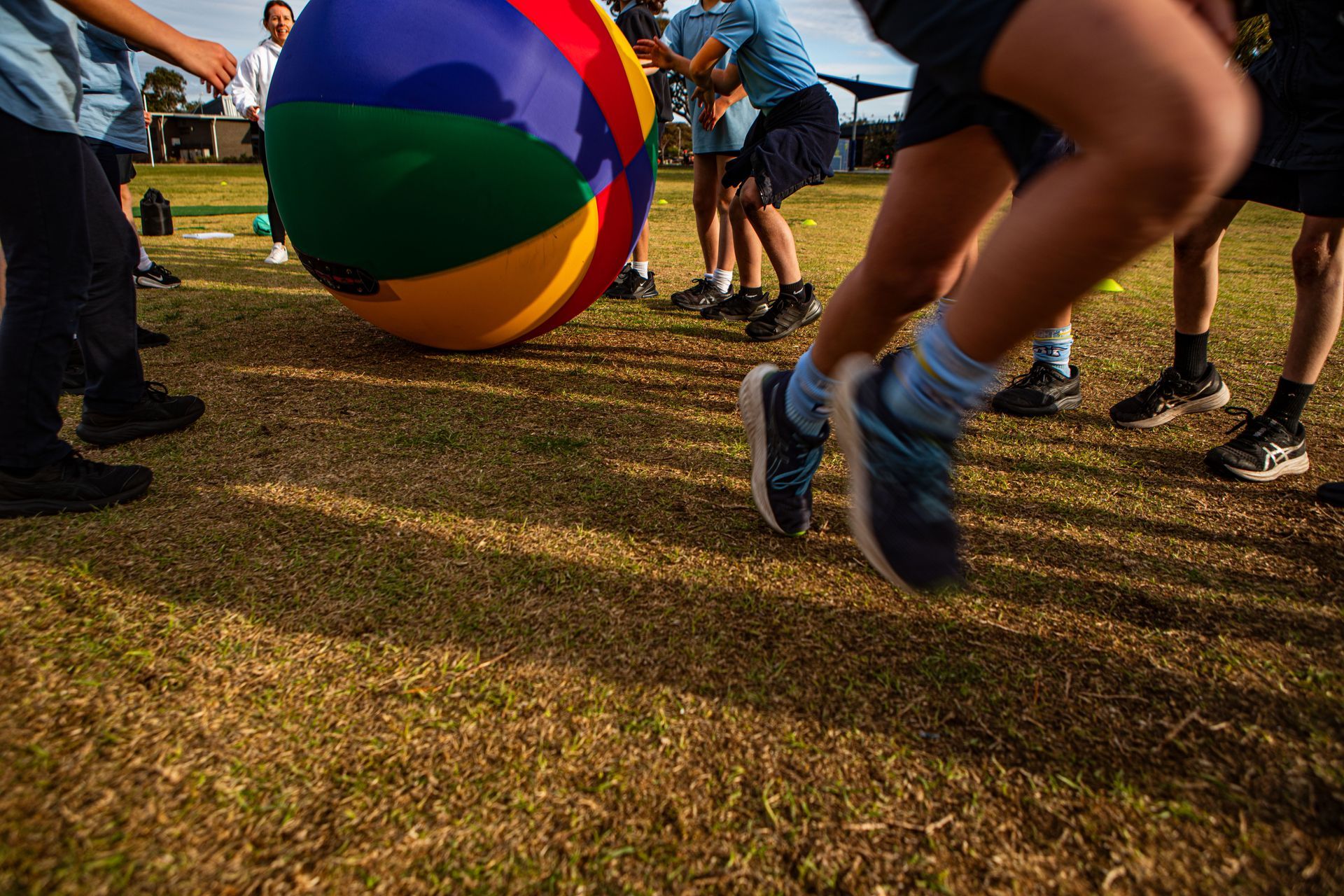 Children playing with a large colorful ball on a grassy field.