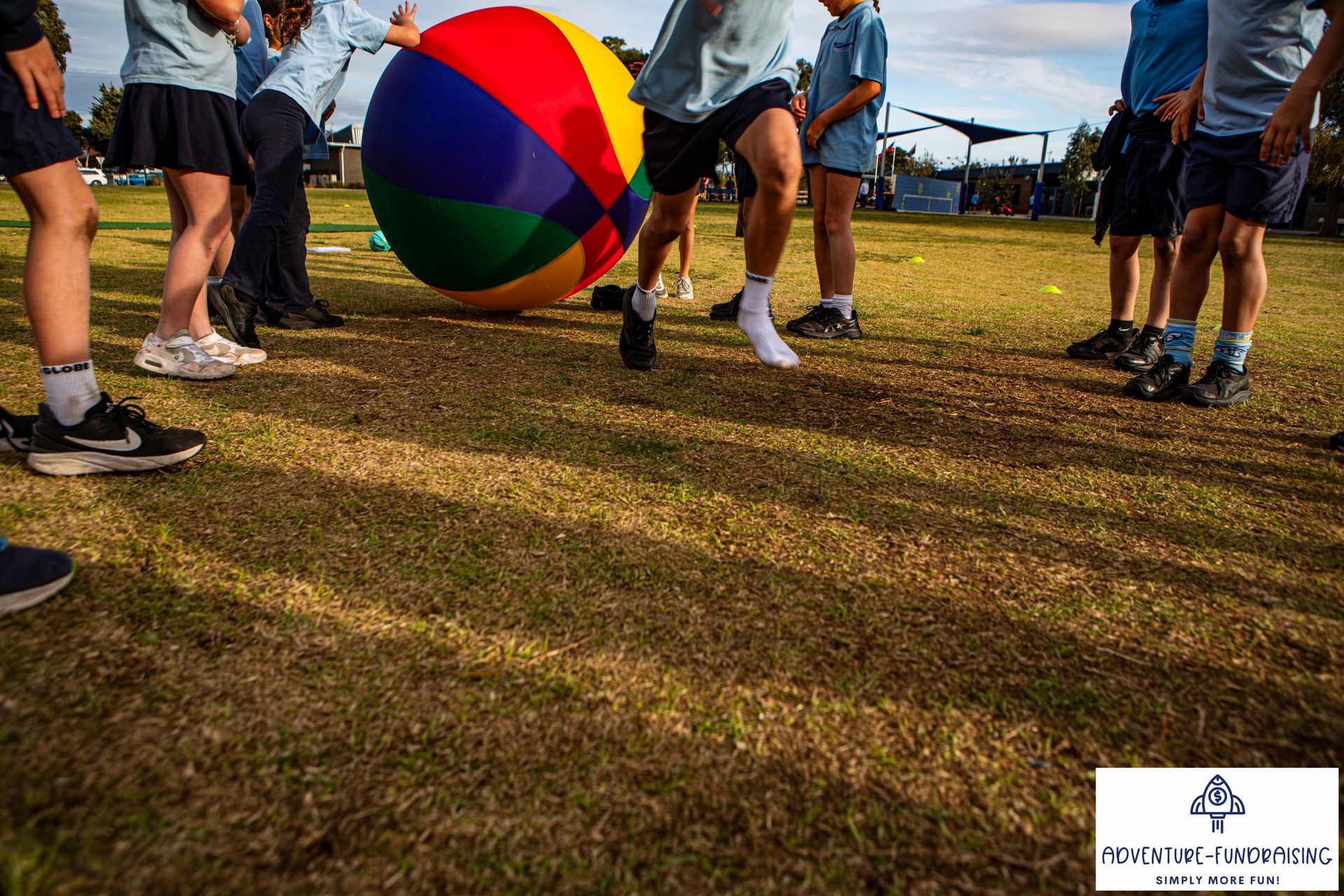 Children playing with a large colorful ball on a grassy field.