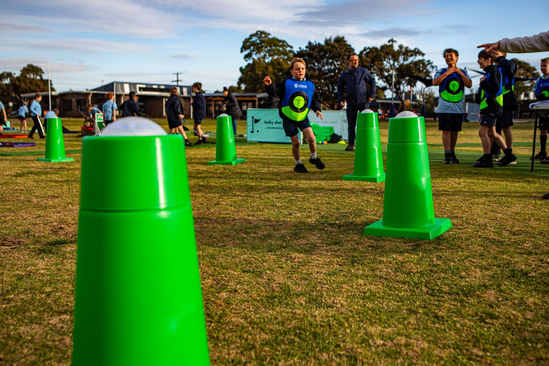 Children playing a game with green cones on a grassy field. Boys wearing matching shirts, one throwing a ball.