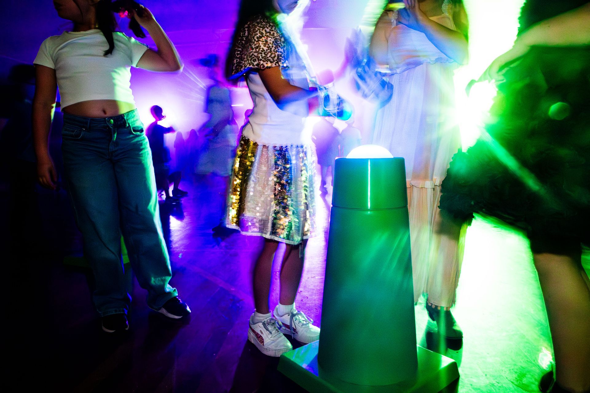 People dancing in a club with colorful lights, including green and purple, shining on them.