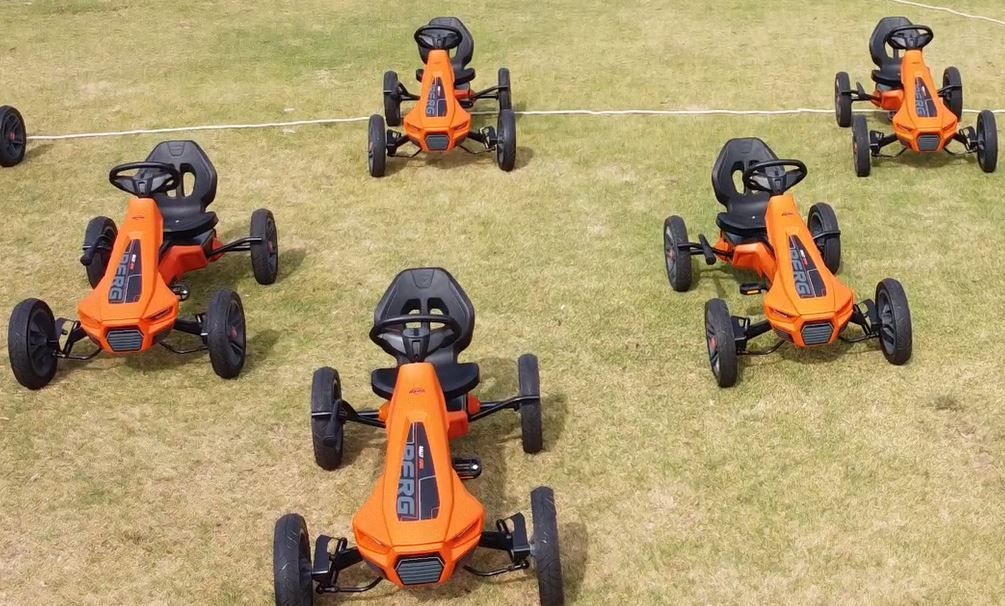 Seven orange go-karts on a grassy field.