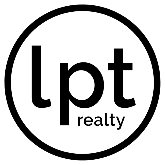 Person at desk with a laptop, books, and plants. A vase with greenery sits on a small stool.