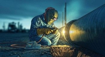 Welder fitting large-diameter pipe section at a midstream right-of-way with open trench