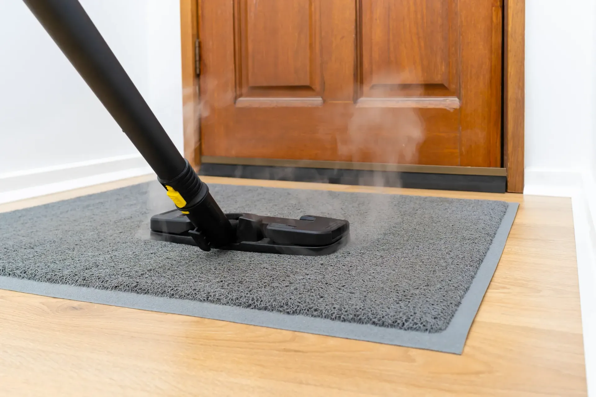 A vacuum cleaner is cleaning a door mat on a wooden floor.