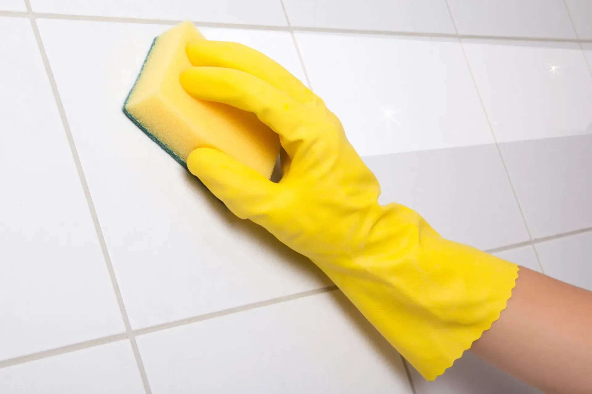 A person wearing a yellow glove is cleaning a tile wall with a sponge