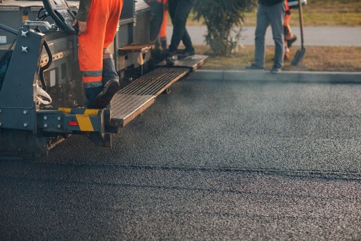 Construction workers paving a road with an asphalt paver machine.