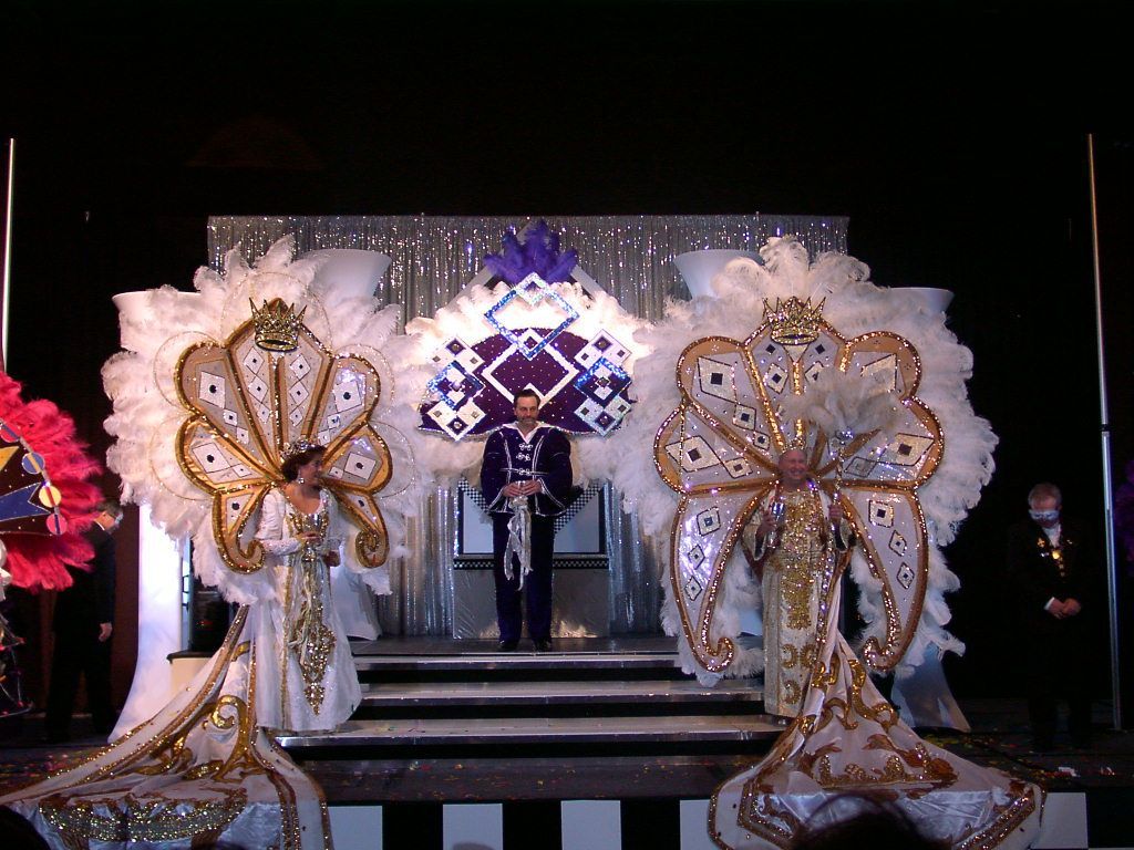 A man stands on a stage surrounded by feathered costumes