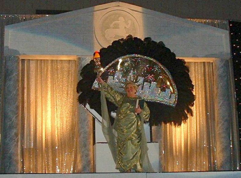 A woman in a gold dress is holding a fan in front of a building