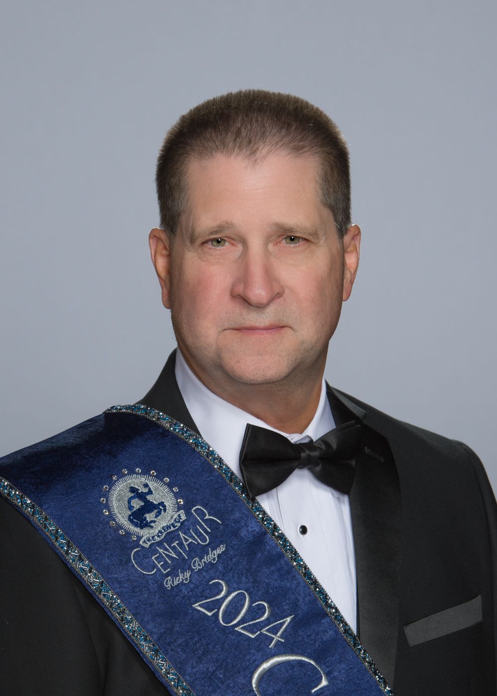 A man in a tuxedo and bow tie is wearing a sash with the year 2024 on it.