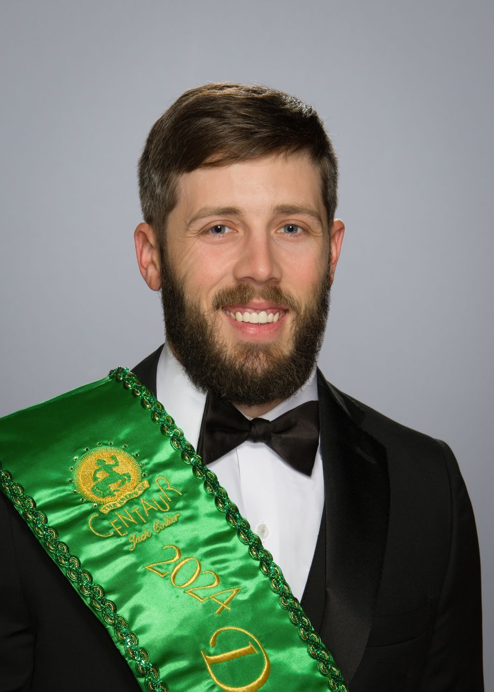 A man with a beard is wearing a green sash and a bow tie.