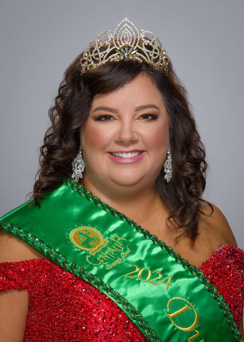 A woman in a red dress is wearing a green sash and a tiara.
