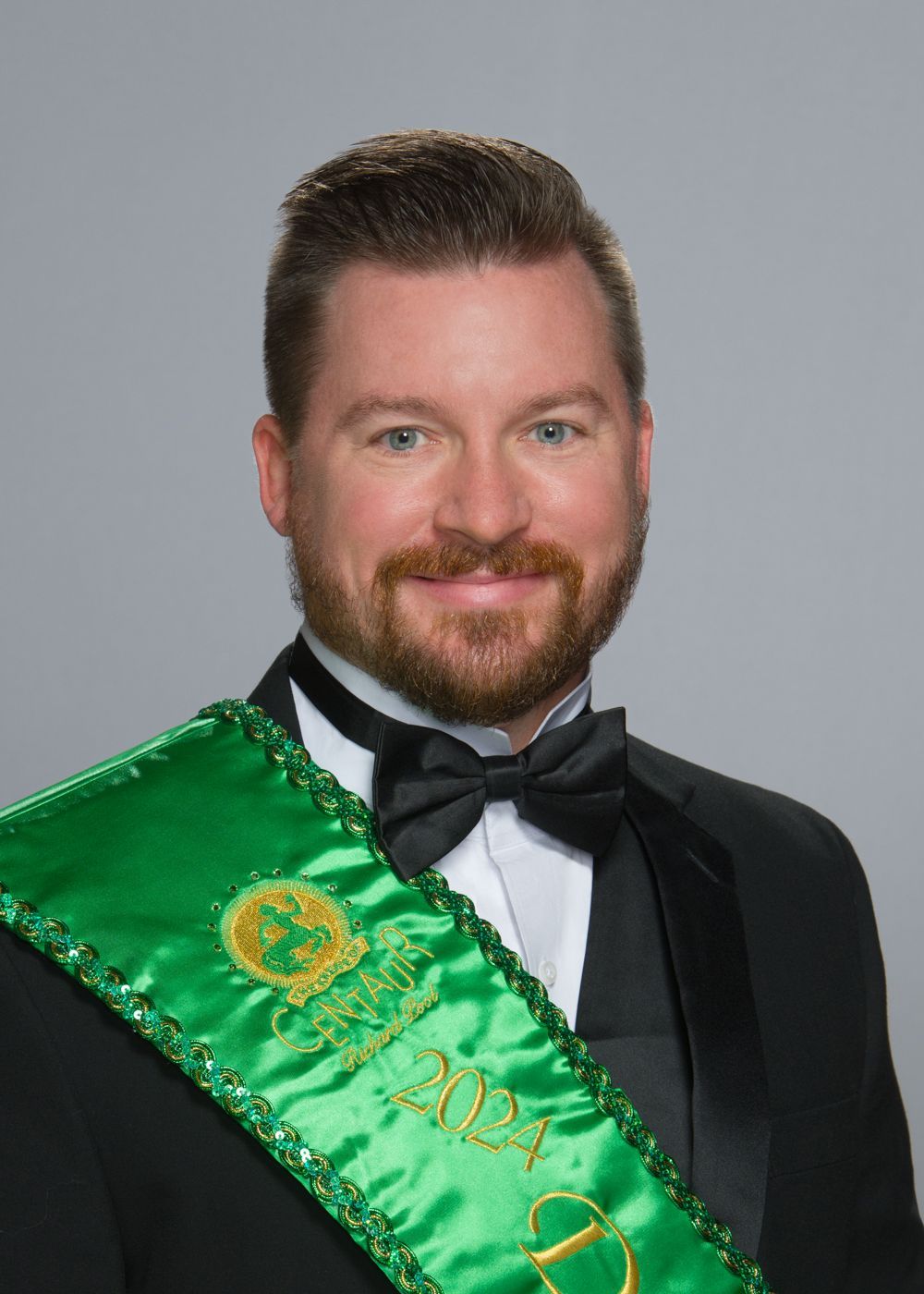 A man in a tuxedo and bow tie is wearing a green sash.