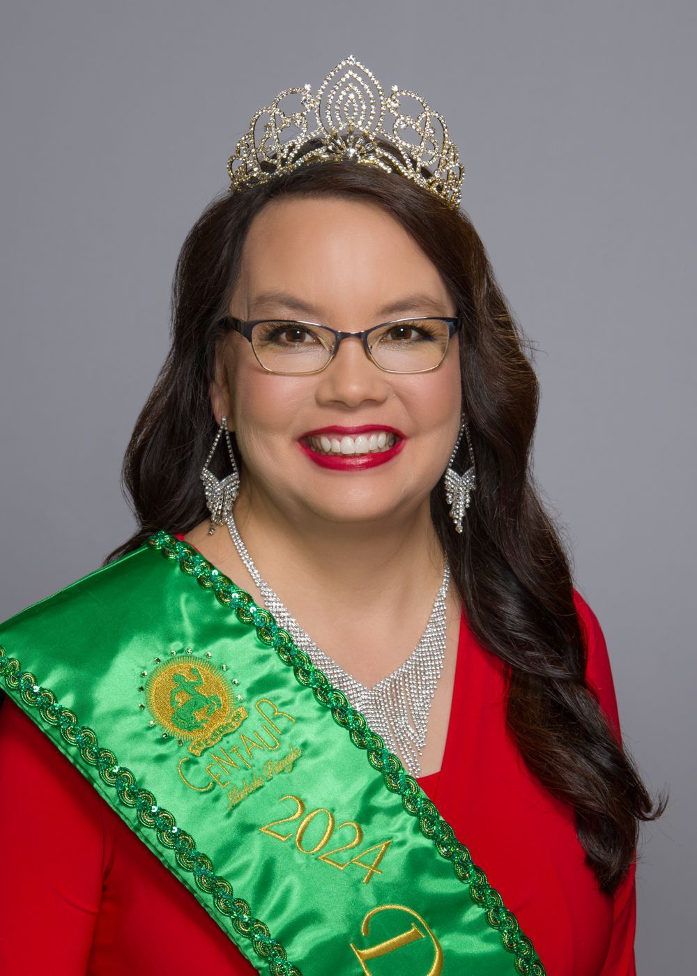 A woman wearing a green sash and a tiara is smiling.