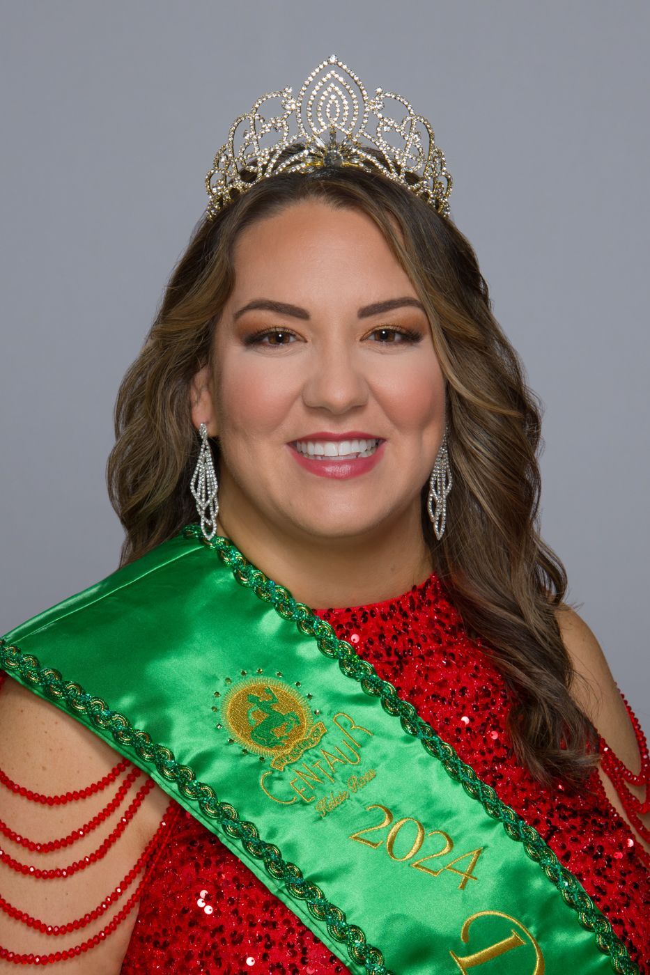 A woman in a red dress is wearing a green sash and a tiara.
