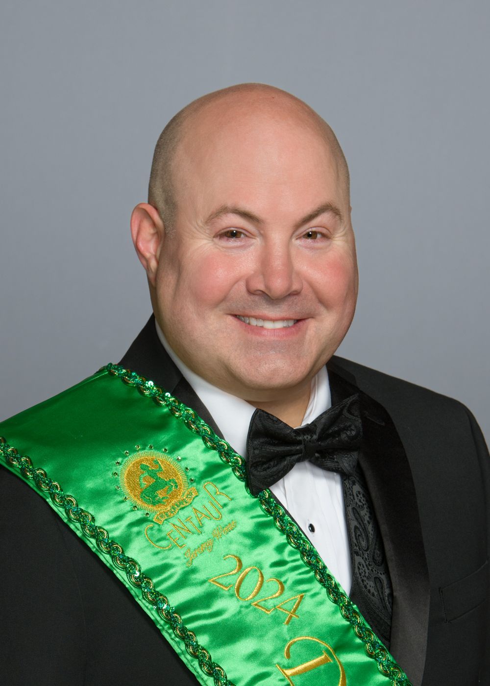 A man in a tuxedo with a green sash around his neck.