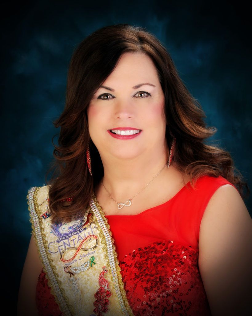 A woman in a red dress and sash is smiling for the camera