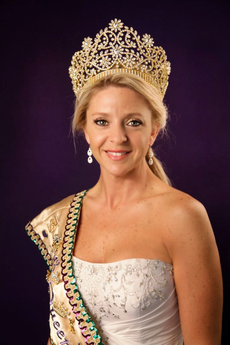 A woman wearing a crown and sash is smiling for the camera