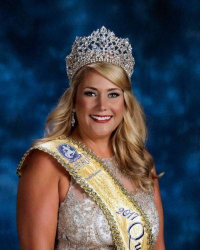 A woman is wearing a crown and sash and smiling.
