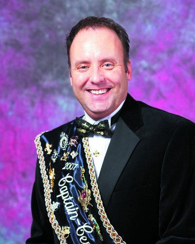 A man in a tuxedo is wearing a sash that says captain bar