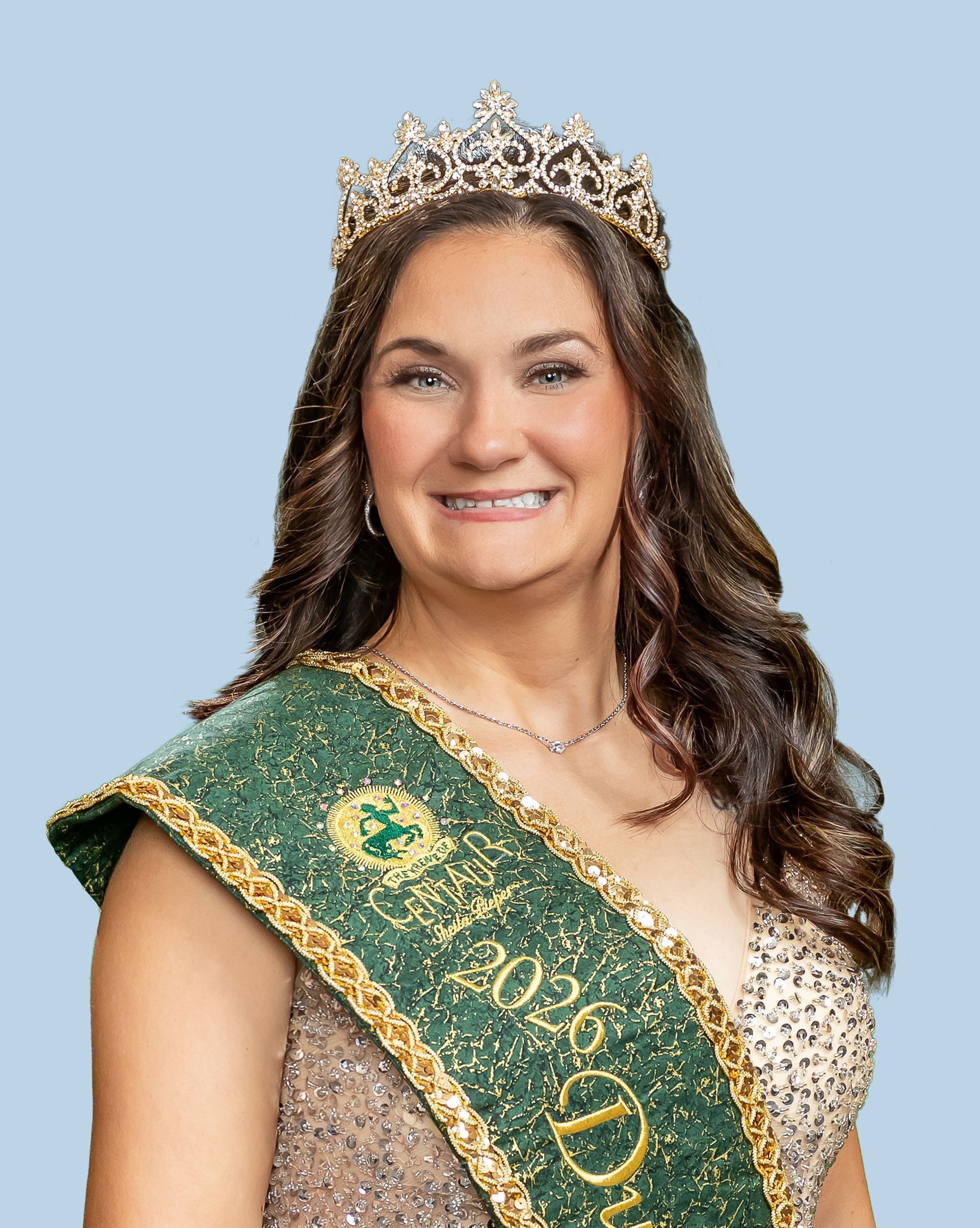 A woman wearing a tiara and a sash is smiling.