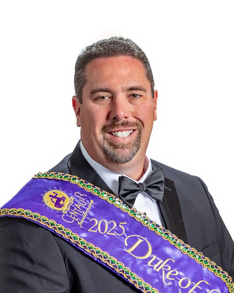 A man in a suit and bow tie is wearing a sash that says duke of