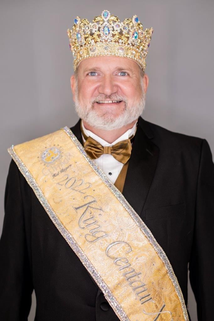 A man in a suit and tie is wearing a crown and sash.