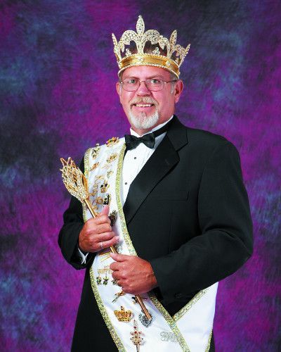 A man in a tuxedo is wearing a crown and holding a wand