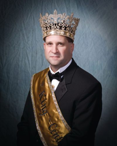 A man wearing a crown and a sash that says king