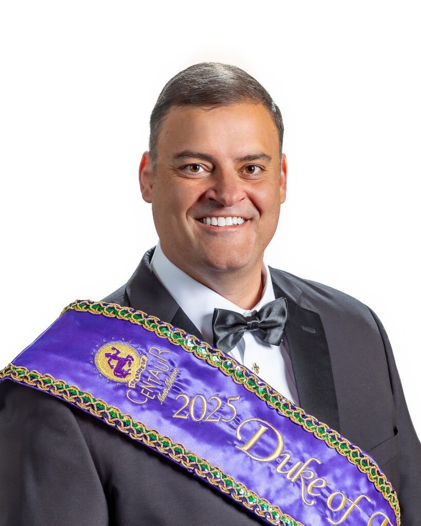 A man in a suit and bow tie is wearing a purple sash.