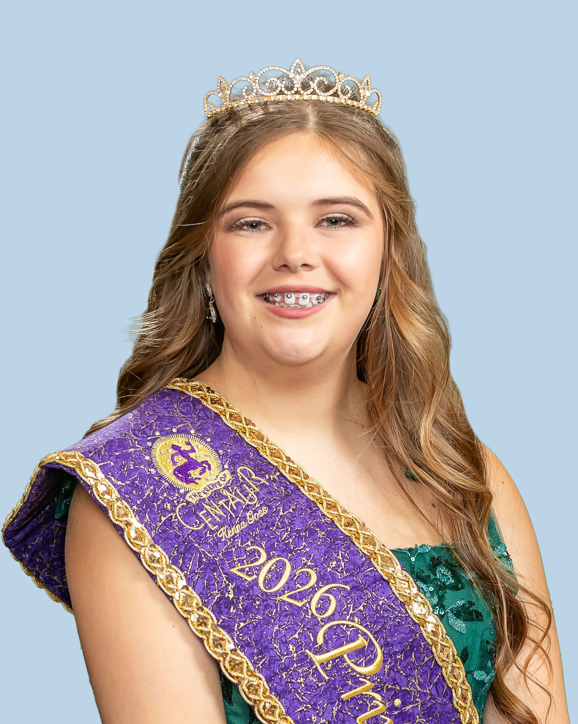A woman in a dress is wearing a purple sash and a tiara and is a princess. 
