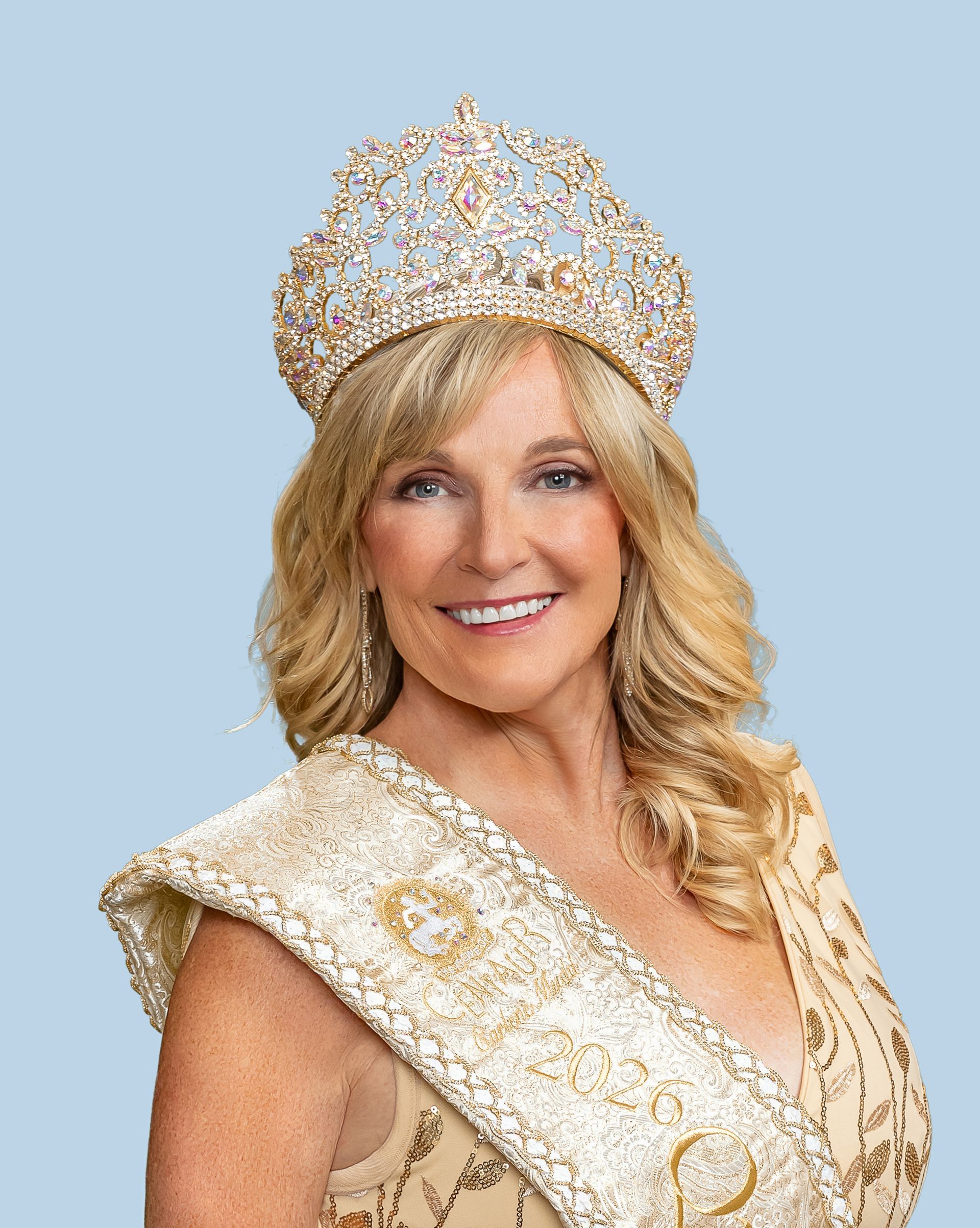 A woman wearing a crown and a sash is smiling and representing the Queen of Centaur. 