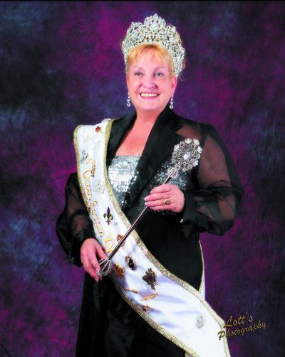 A woman wearing a tiara and sash is smiling and holding a wand